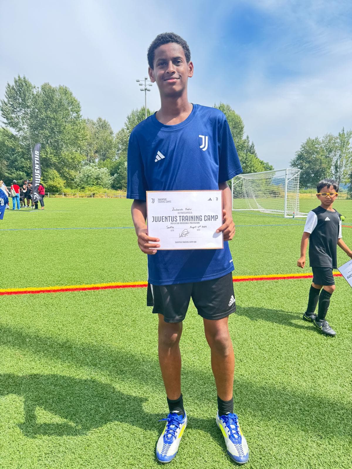 Zecheriah holding his Juventus Training Camp certificate on the pitch in Seattle, August 2023